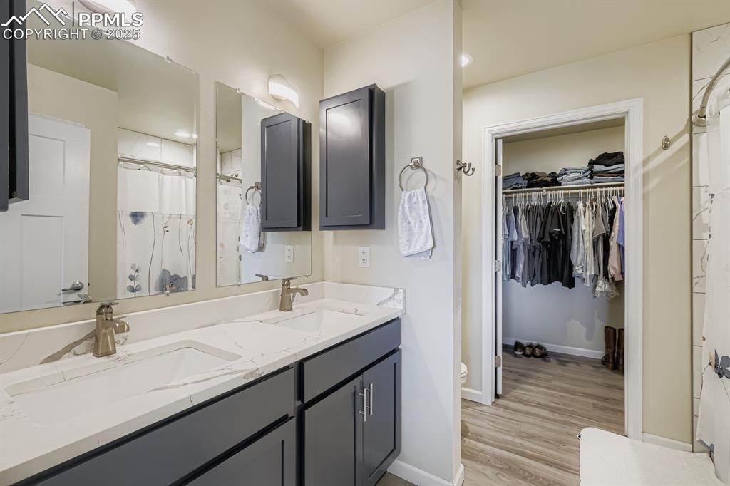 Bathroom featuring a shower with shower curtain, double vanity, a walk in closet, light wood-type flooring, and recessed lighting