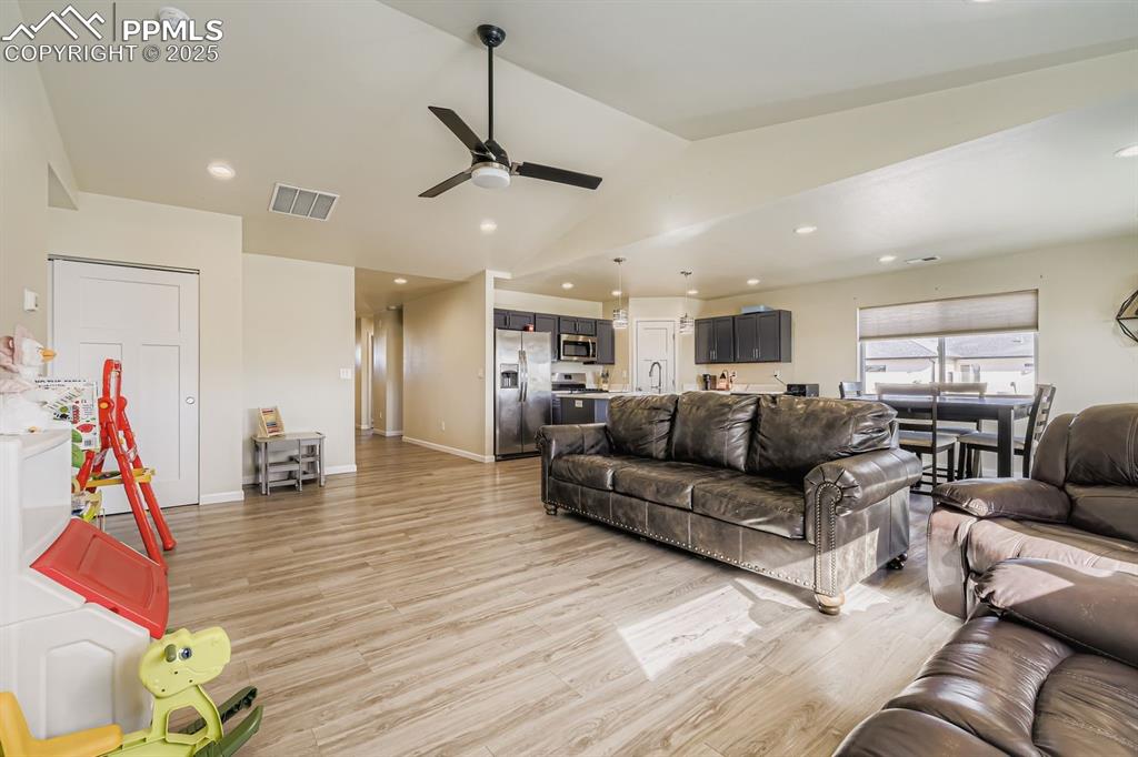 Living room featuring light wood-style flooring, vaulted ceiling, ceiling fan, and recessed lighting