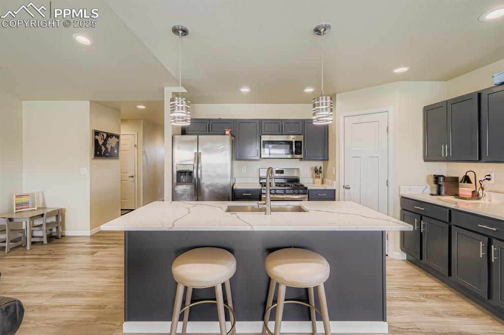 Kitchen with hanging light fixtures, a kitchen bar, stainless steel appliances, light wood-style flooring, and recessed lighting