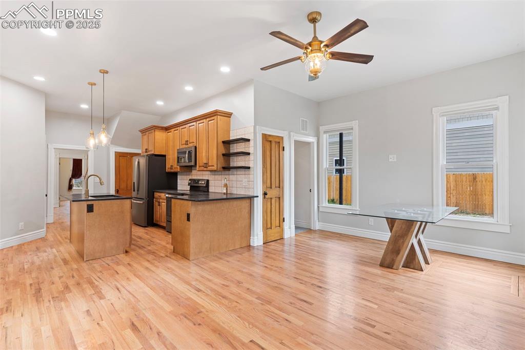 Kitchen with tasteful backsplash, hanging light fixtures, a center island with sink, light wood finished floors, and range with electric cooktop