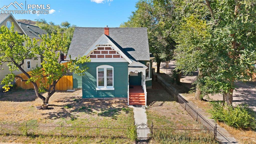 View of front of home featuring a chimney, brick siding, a fenced front yard, and roof with shingles