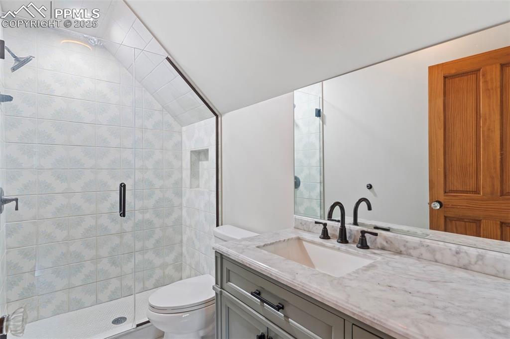 Bathroom featuring a shower stall, vanity, and vaulted ceiling