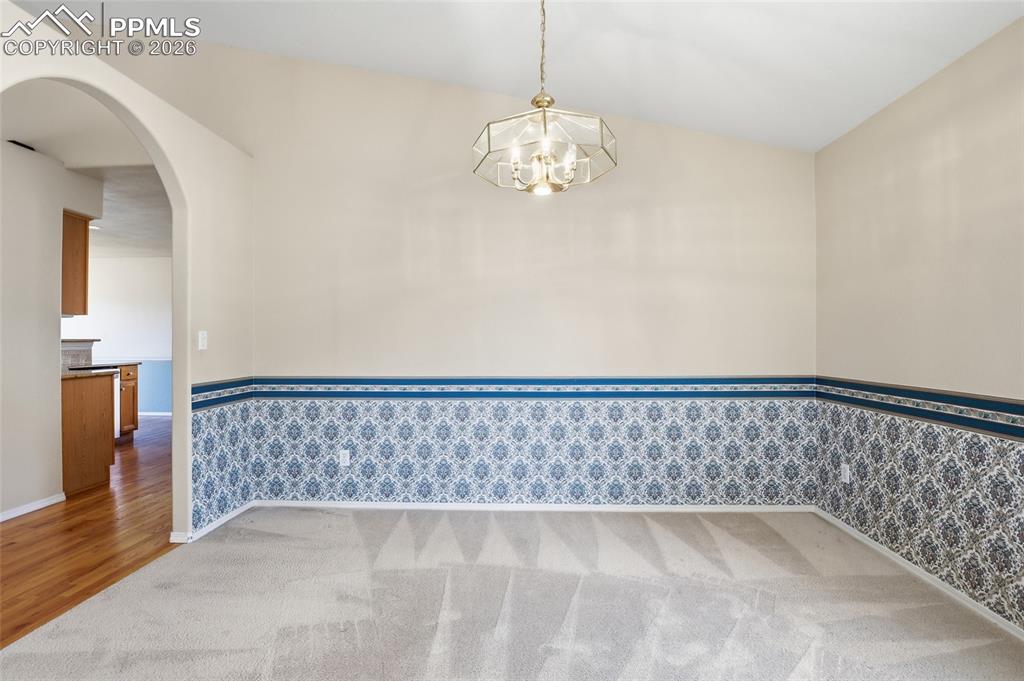 Spare room with arched walkways, hanging lights, light colored carpet, wainscoting, and wallpapered walls