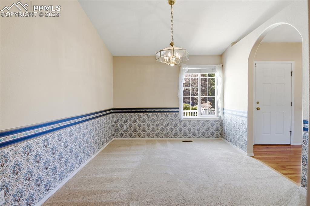 Spare room featuring arched walkways, wainscoting, suspended lighting, wallpapered walls, and carpet