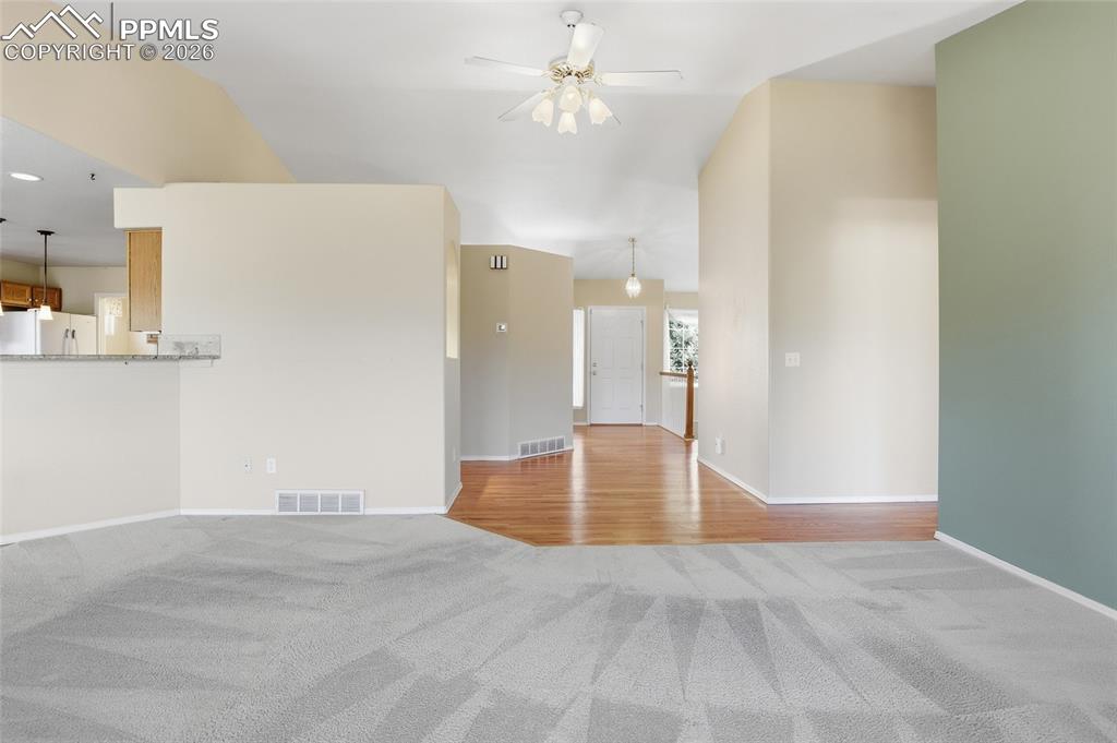 Unfurnished living room with light colored carpet, ceiling fan, and lofted ceiling