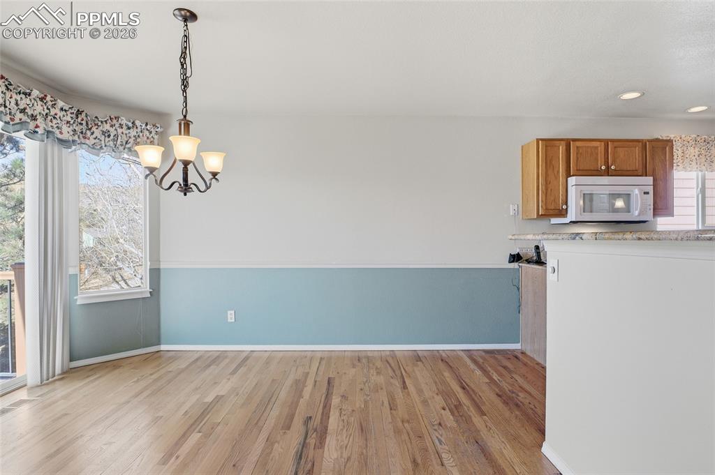 Kitchen featuring light wood-style flooring, white microwave, a chandelier, wood finish cabinetry, and light stone countertops