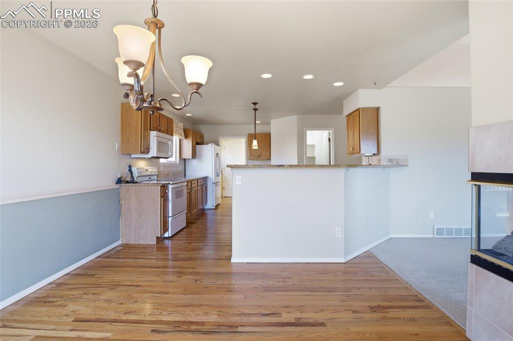 Kitchen with wood finish cabinets, white appliances, a peninsula, light wood finished floors, and a chandelier