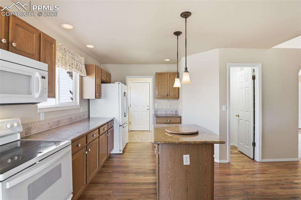 Kitchen featuring white appliances, wood finish cabinetry, and dark wood-style flooring