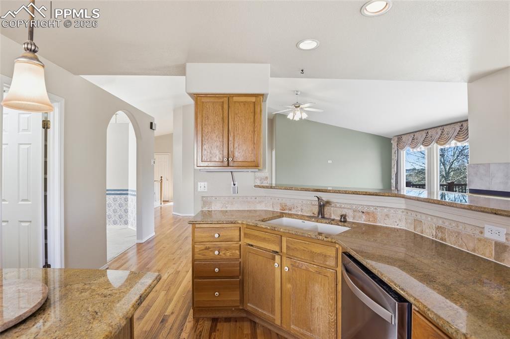 Kitchen featuring light stone countertops, stainless steel dishwasher, arched walkways, light wood-style flooring, and vaulted ceiling