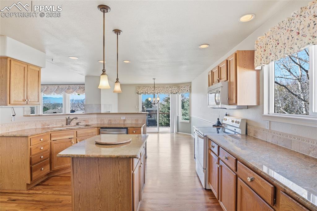Kitchen featuring white range with electric stovetop, a peninsula, a kitchen island, light stone counters, and a chandelier