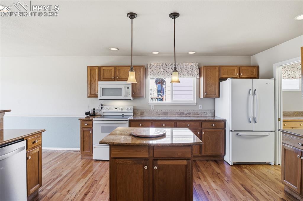 Kitchen featuring white appliances, a kitchen island, wood finish cabinets, and dark stone counters