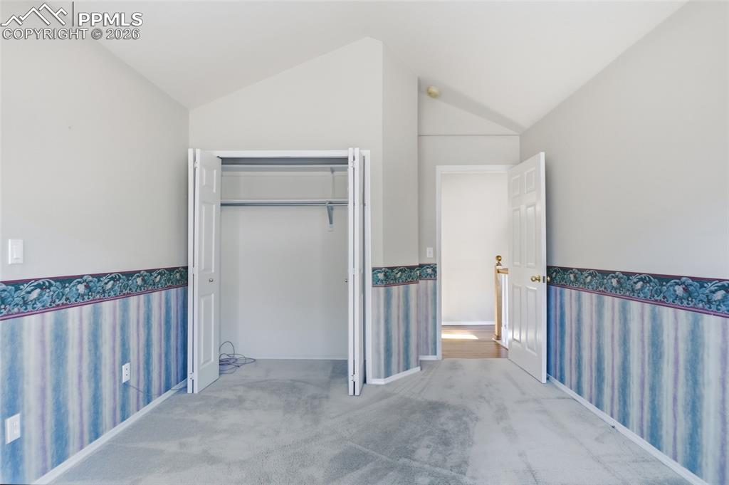 Unfurnished bedroom with wallpapered walls, wainscoting, lofted ceiling, light carpet, and a closet