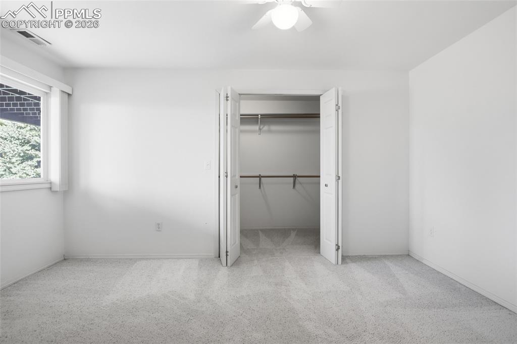 Unfurnished bedroom with light carpet, a walk in closet, and a ceiling fan