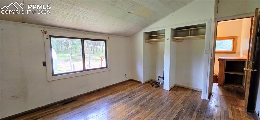 Unfurnished bedroom featuring hardwood / wood-style floors, lofted ceiling, and a closet