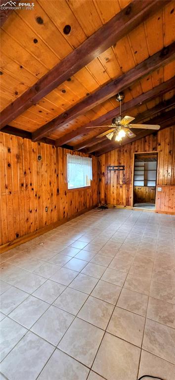 Unfurnished living room with light tile patterned flooring, a wood ceiling with exposed beams, wooden walls, and ceiling fan