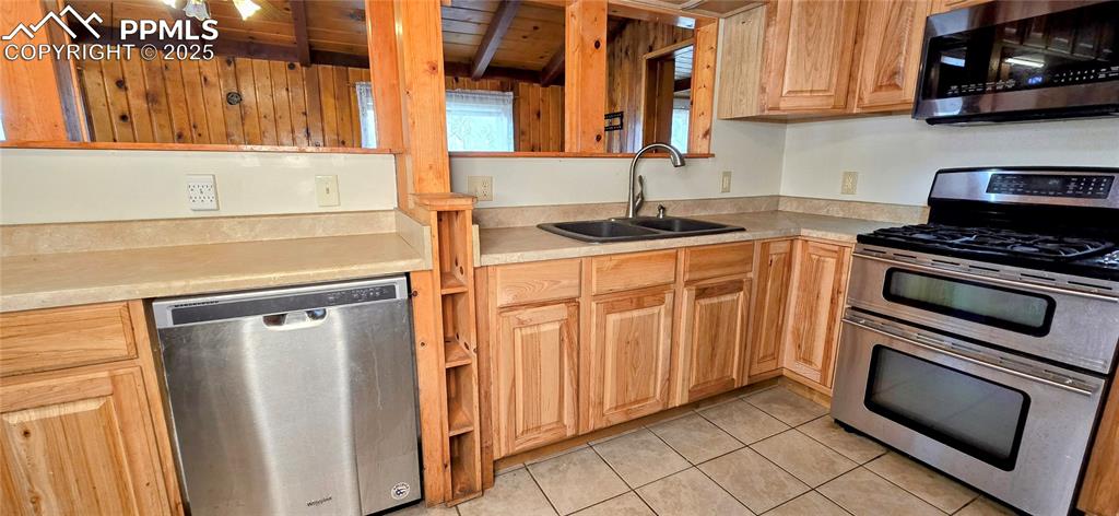 Kitchen with appliances with stainless steel finishes, light countertops, light tile patterned floors, and a wooden ceiling with exposed beams