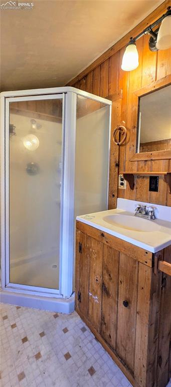Bathroom with wood walls, a stall shower, vanity, and tile patterned floors