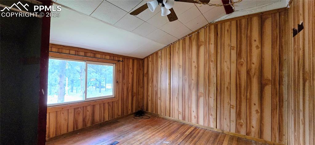 Spare room with hardwood / wood-style flooring, wood walls, ceiling fan, and lofted ceiling