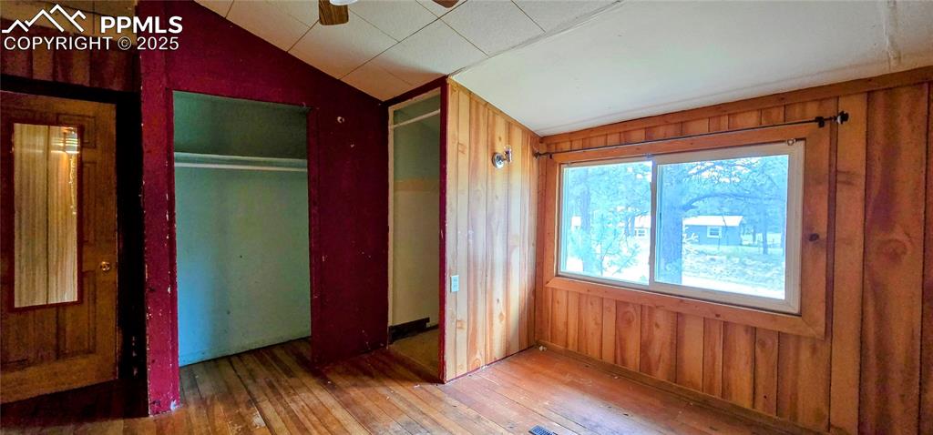 Unfurnished bedroom with lofted ceiling, wood walls, hardwood / wood-style floors, and a closet