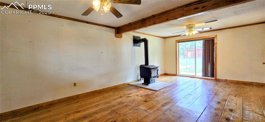 Spare room featuring a ceiling fan, beamed ceiling, hardwood / wood-style floors, a wood stove, and a textured ceiling
