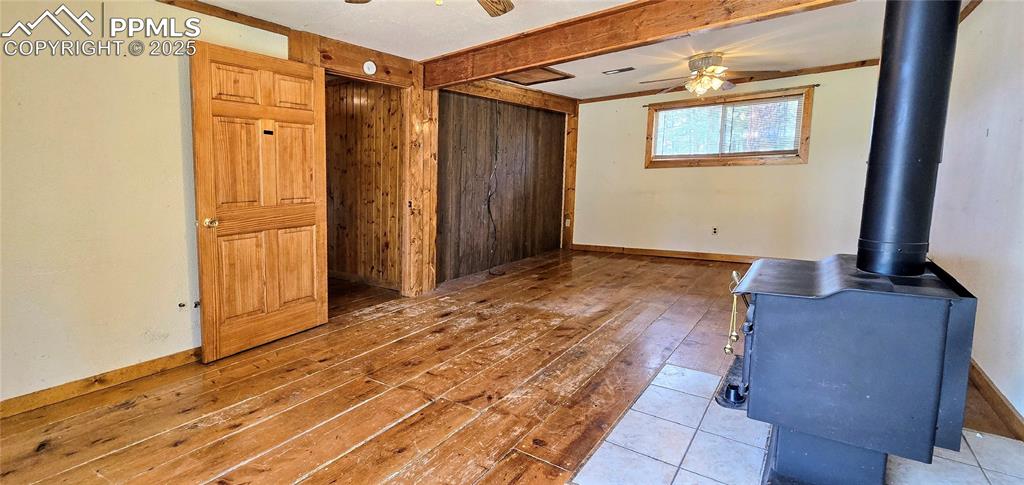Unfurnished living room featuring ceiling fan, hardwood / wood-style flooring, a wood stove, wooden walls, and beamed ceiling