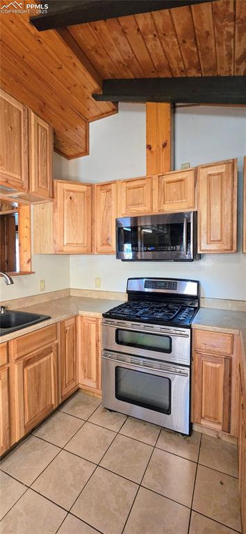 Kitchen featuring appliances with stainless steel finishes, light tile patterned flooring, wooden ceiling, light countertops, and light brown cabinetry