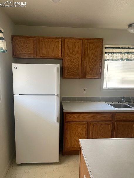 Kitchen featuring brown cabinets, light countertops, freestanding refrigerator, and light flooring