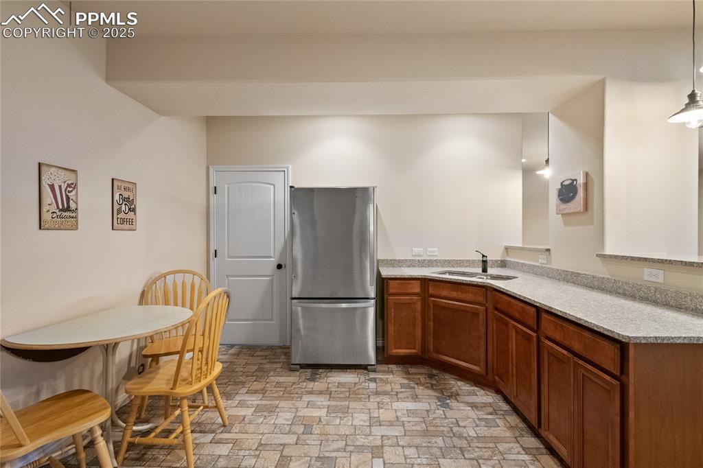 Lower level wet bar with tile flooring, granite counter, full-sized fridge, disposal and pendant lighting. Doorway into storage area. 