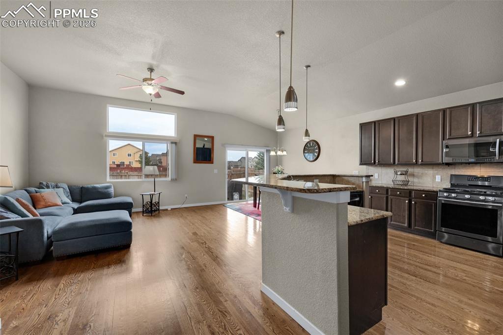 Kitchen featuring stainless steel appliances, open floor plan, a ceiling fan, hardwood flooring, pendant lighting, and granite counters
