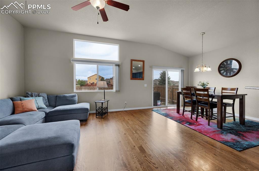 Living room with oak hardwood flooring, ceiling fan, and vaulted ceiling,
