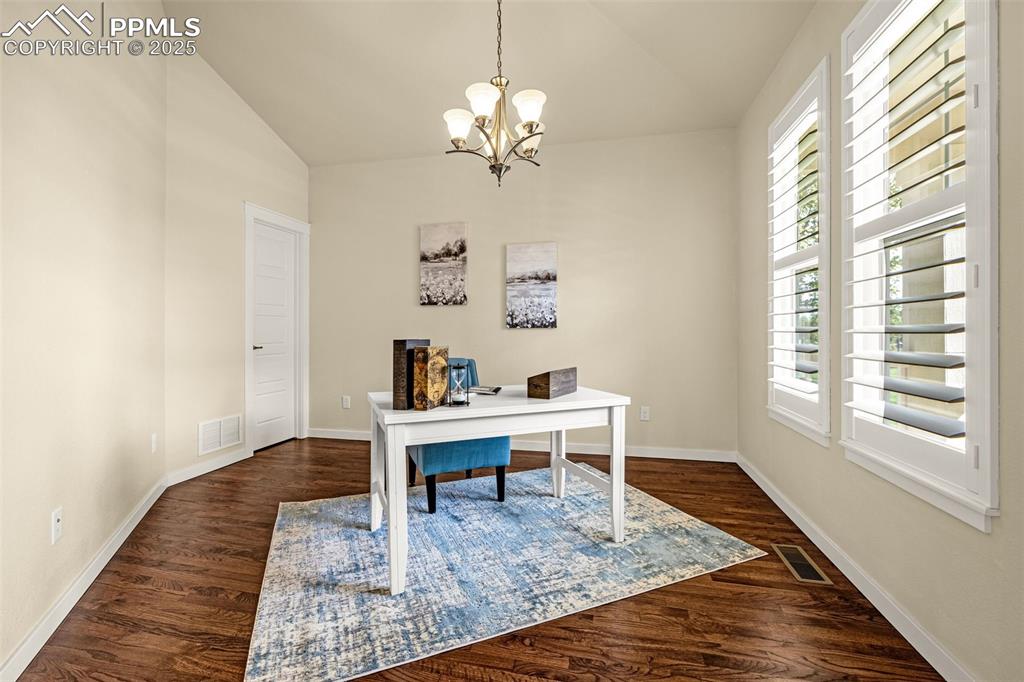 Office area featuring dark hardwood flooring, lofted ceiling, and a chandelier