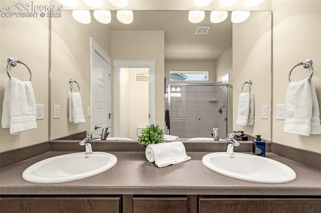 Bathroom with a stall shower, a textured wall, and double vanity
