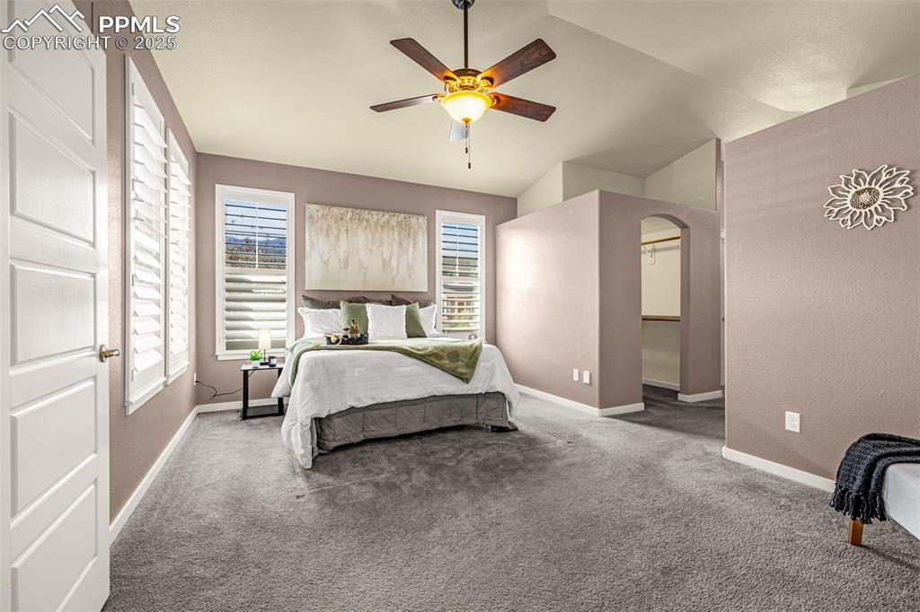 Bedroom featuring carpet flooring, ceiling fan, vaulted ceiling, and arched walkways