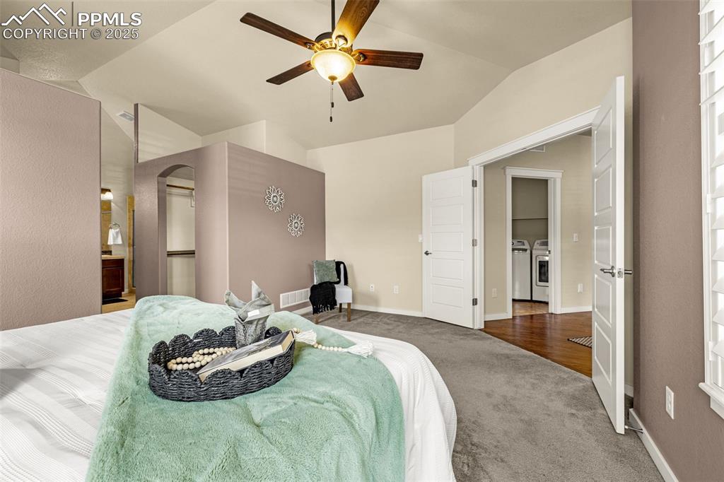 Bedroom with carpet flooring, vaulted ceiling, a ceiling fan, washing machine and clothes dryer, and ensuite bath