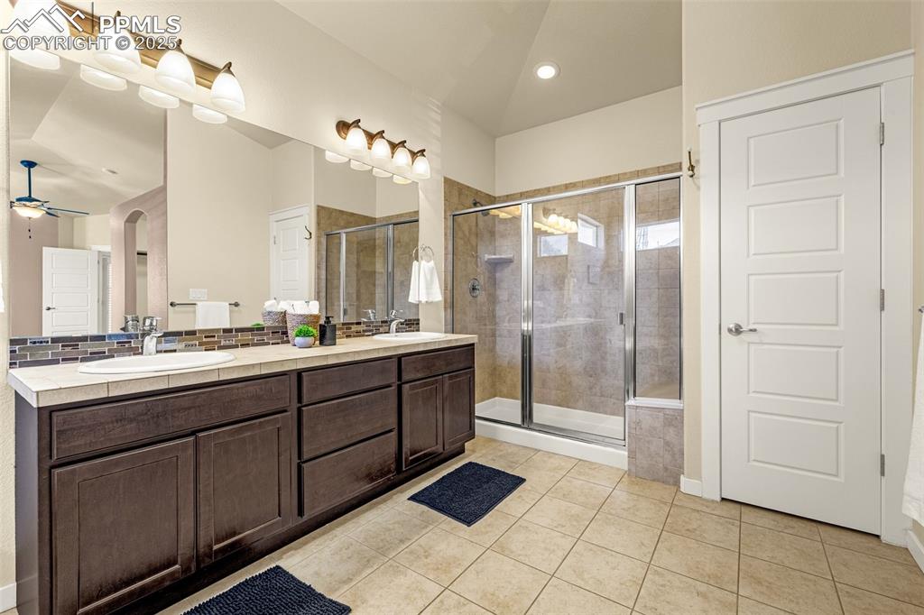 Full bath featuring light tile patterned flooring, double vanity, a shower stall, a ceiling fan, and recessed lighting