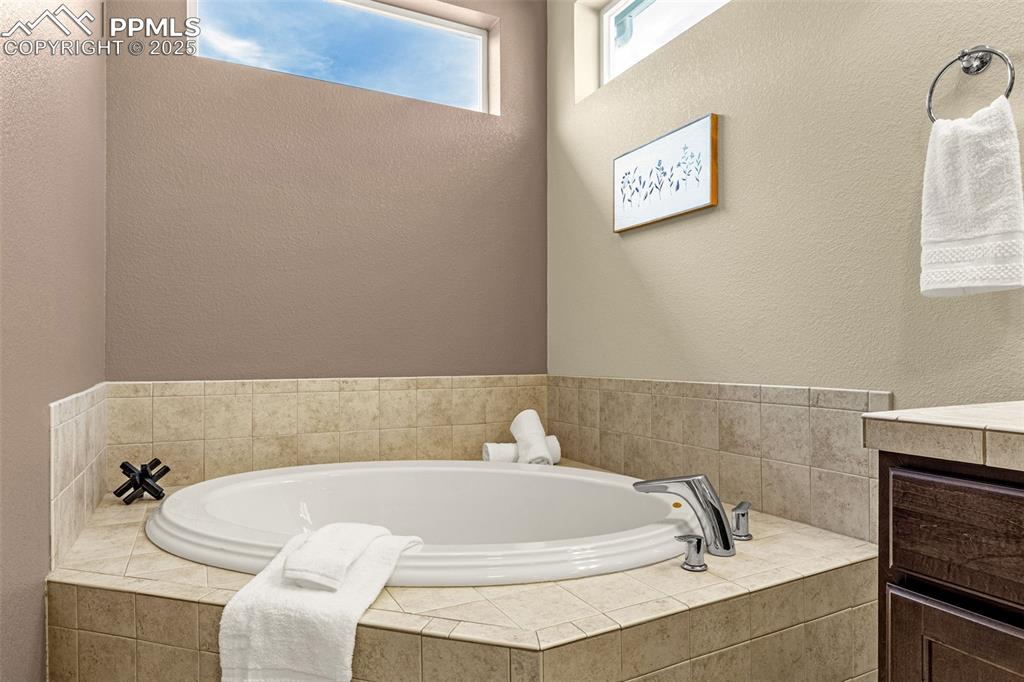 Full bath with a textured wall, a garden tub, and vanity