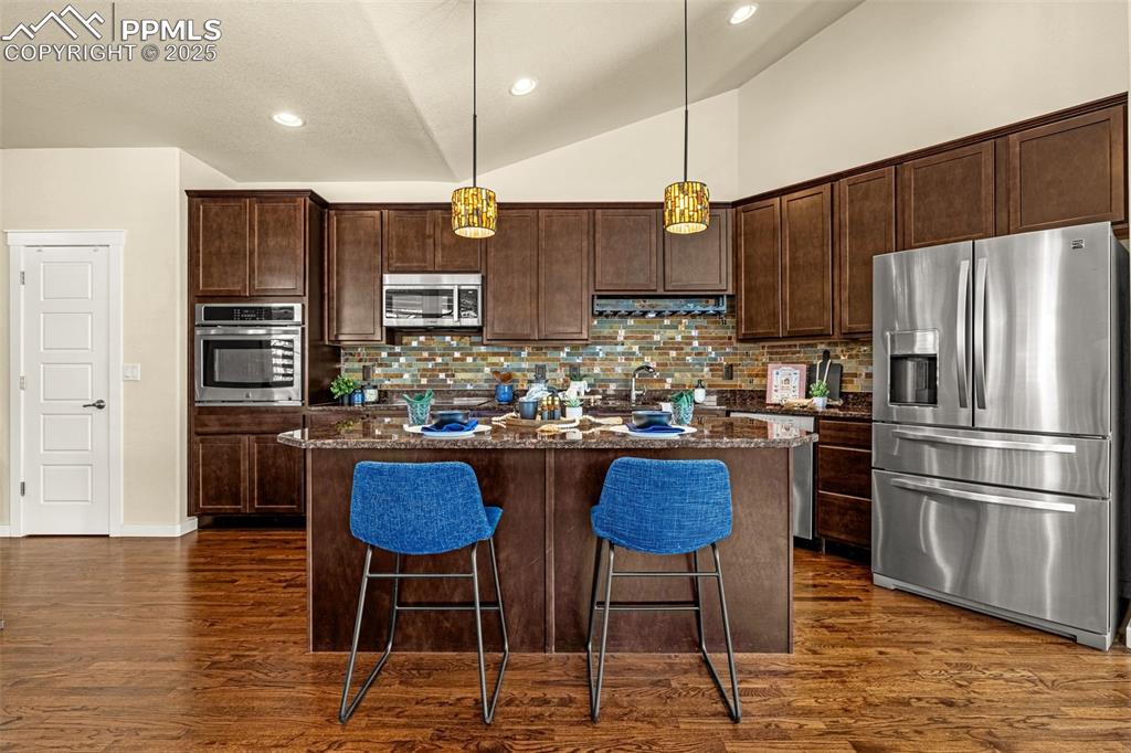 Kitchen featuring stainless steel appliances, pendant lighting, dark brown cabinets, a center island, and vaulted ceiling