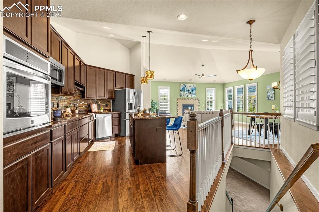 Kitchen featuring dark hardwood flooring, vaulted ceiling, stainless steel appliances, tasteful backsplash, and a center island