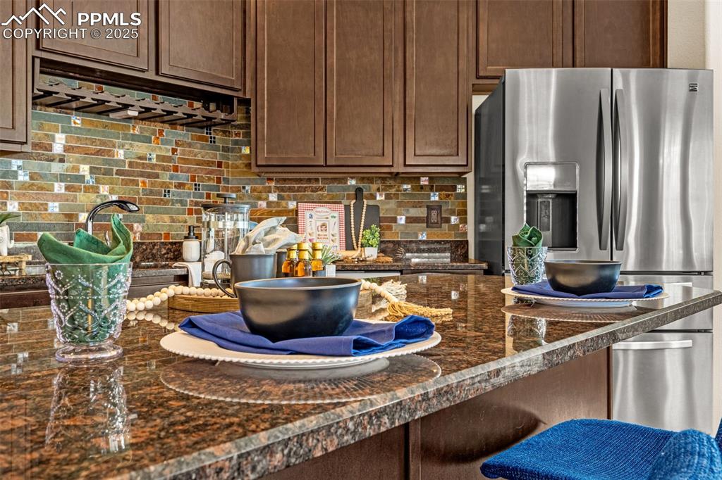 Kitchen featuring decorative backsplash, stainless steel fridge, dark stone countertops, a kitchen breakfast bar, and dark brown cabinetry