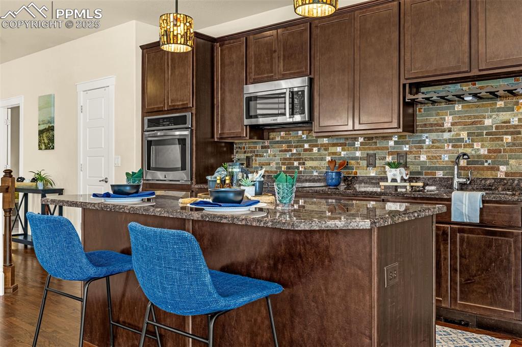 Kitchen with a kitchen bar, tasteful backsplash, dark stone countertops, dark brown cabinetry, and stainless steel appliances