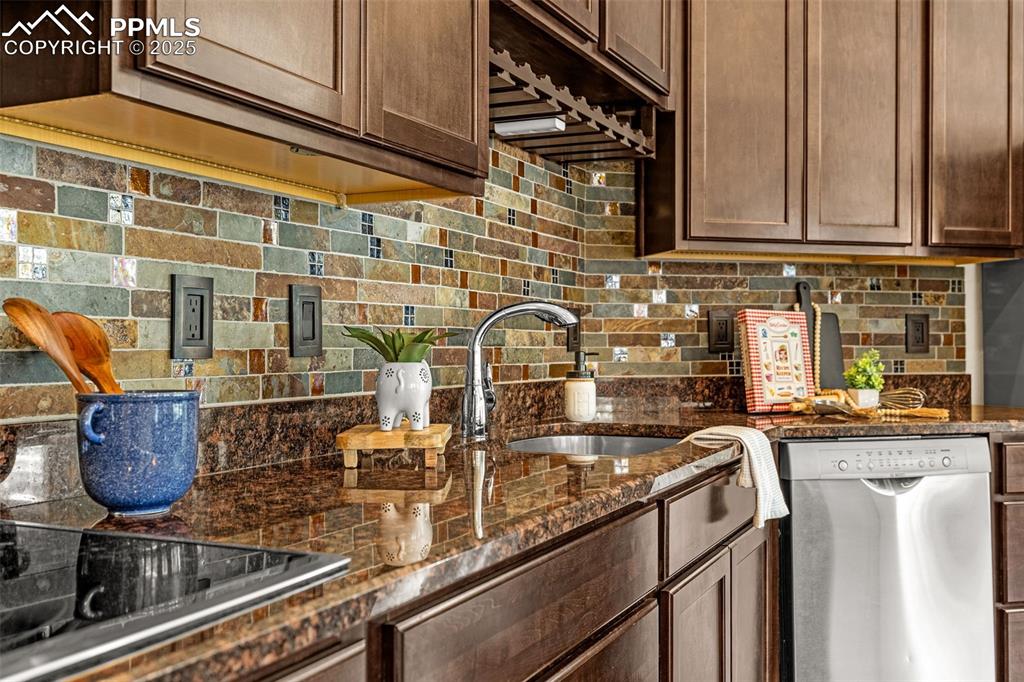 Kitchen with stainless steel dishwasher, tasteful backsplash, black electric stovetop, dark brown cabinets, and dark stone countertops