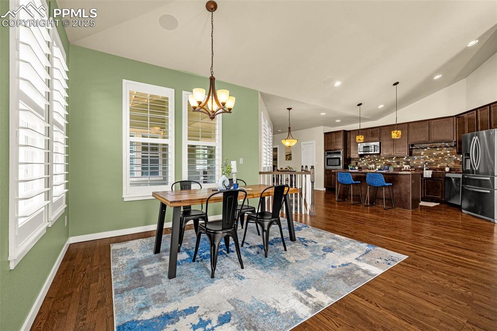 Dining space with vaulted ceiling, a chandelier, dark hardwood flooring, and recessed lighting