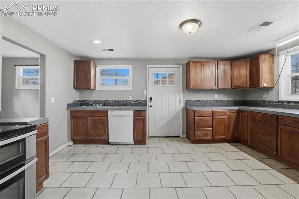 Kitchen featuring dishwasher, brown cabinetry, range with two ovens, and dark countertops