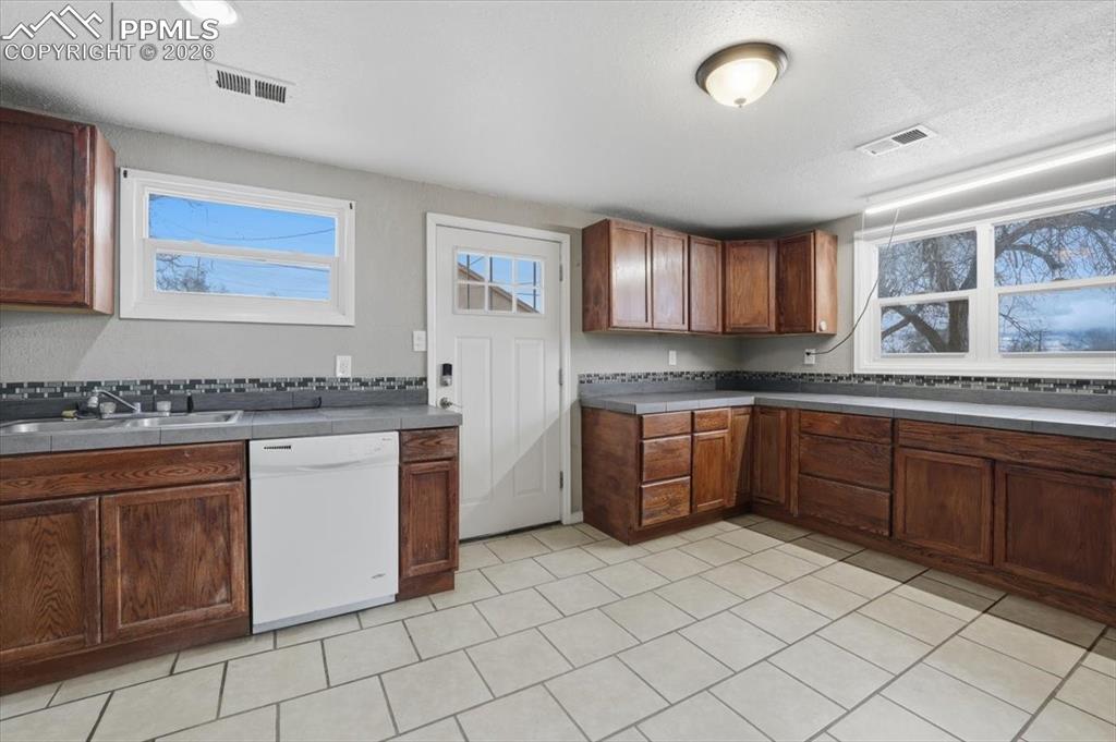 Kitchen featuring white dishwasher, a textured ceiling, brown cabinets, and light tile patterned floors