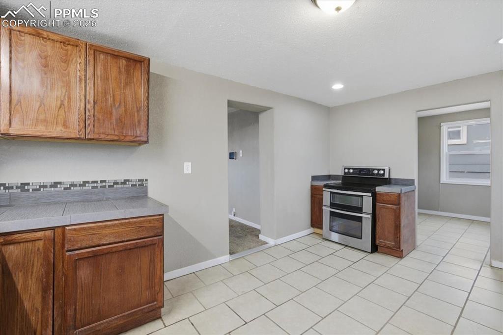 Kitchen featuring range with two ovens, brown cabinets, light tile patterned flooring, tile counters, and recessed lighting