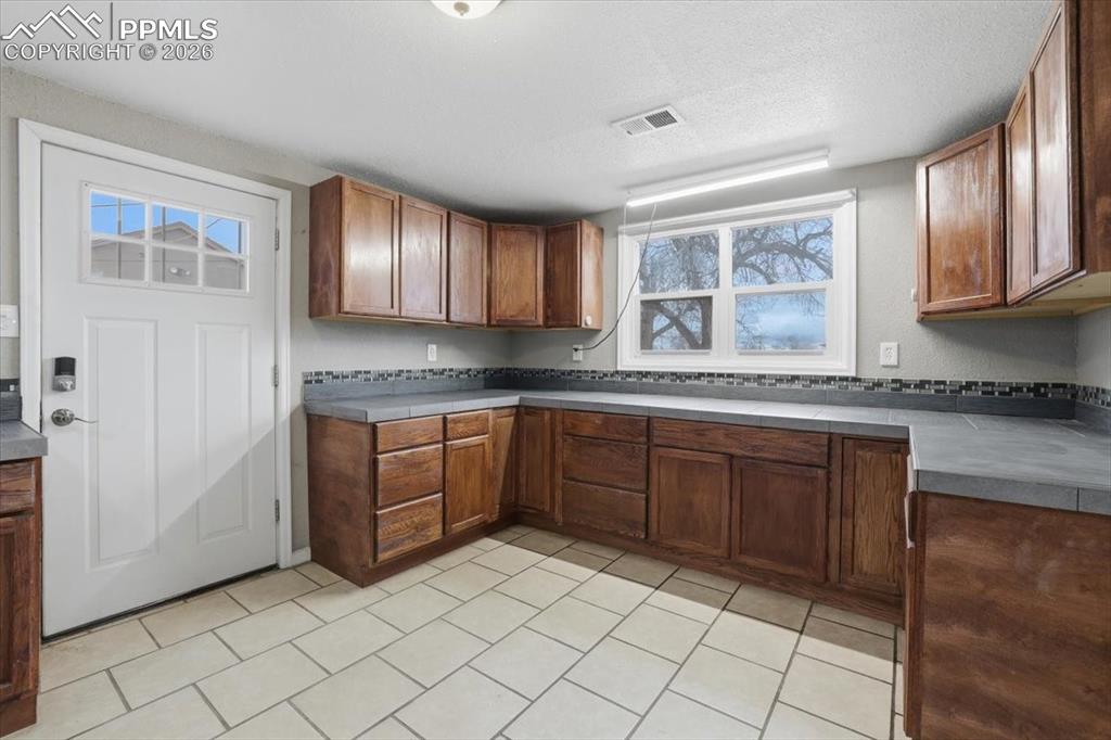Kitchen featuring brown cabinetry, dark countertops, a textured ceiling, and light tile patterned floors