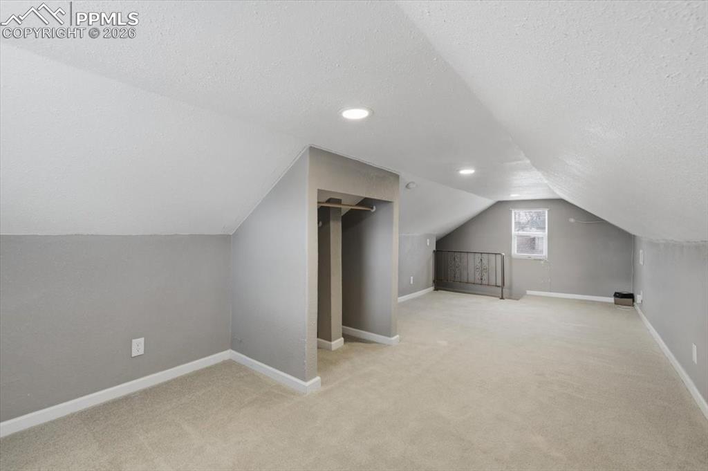 Additional living space with a textured ceiling, lofted ceiling, light colored carpet, and recessed lighting