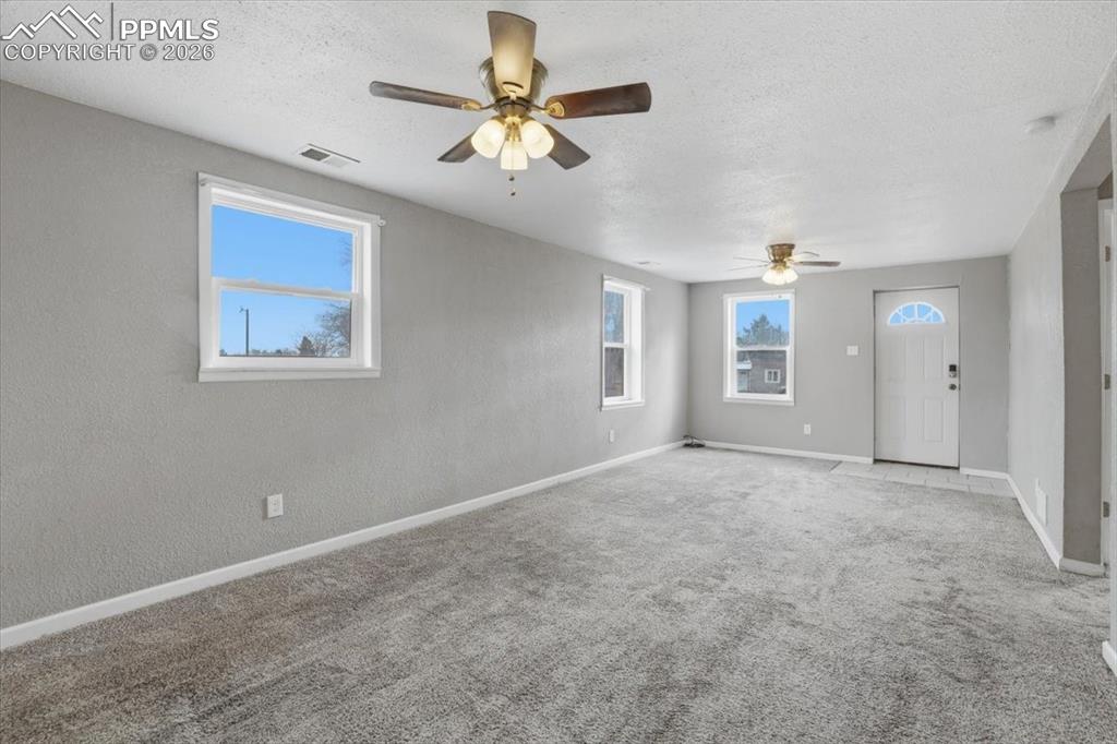 Carpeted empty room with healthy amount of natural light, a textured ceiling, and a ceiling fan