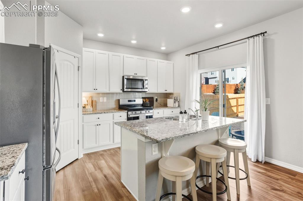 Kitchen featuring appliances with stainless steel finishes, a breakfast bar area, light wood-type flooring, decorative backsplash, and recessed lighting