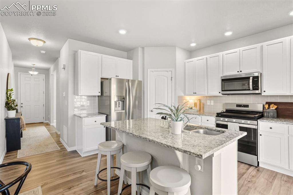 Kitchen with stainless steel appliances, white cabinetry, light stone counters, light wood-type flooring, and recessed lighting